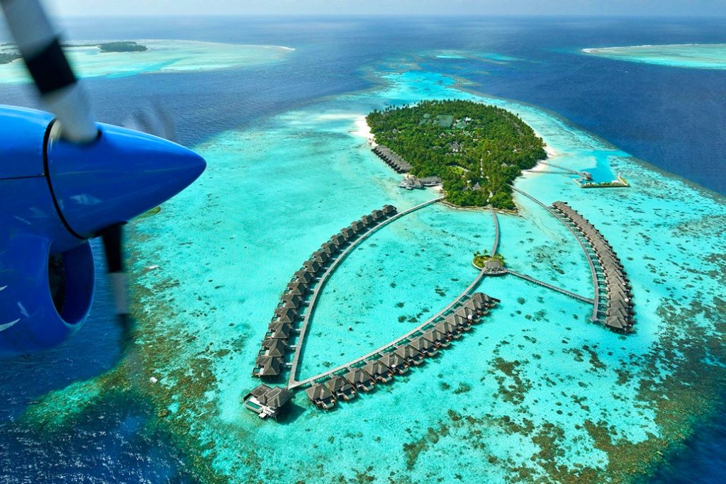 Aerial perspective of a luxury resort island with wooden overwater villas and crystal clear turquoise lagoon in Dhaalu Atoll, Maldives.