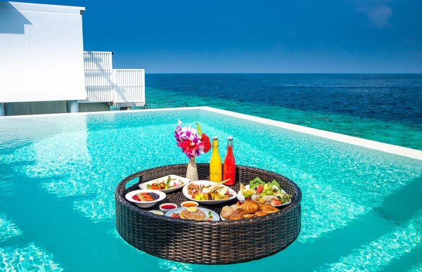 A luxury floating breakfast tray with tropical fruits and coffee in a turquoise private pool at a Noonu Atoll resort, Maldives.