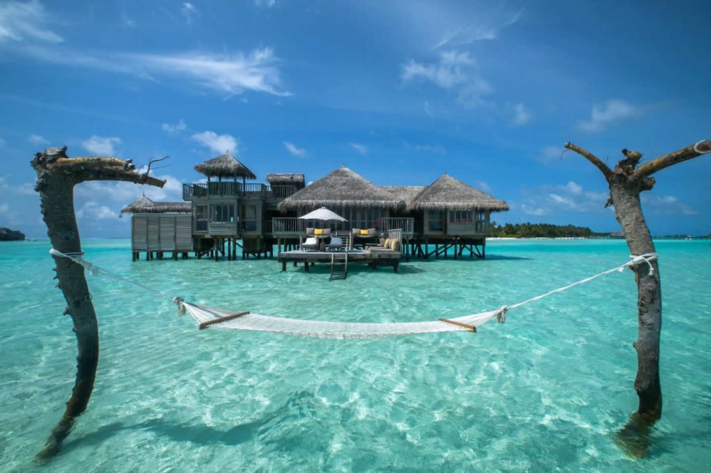 A luxury overwater hammock in crystal clear turquoise water at Gili Lankanfushi resort, showcasing a famous Instagram spot in the Maldives with overwater villas in the background.
