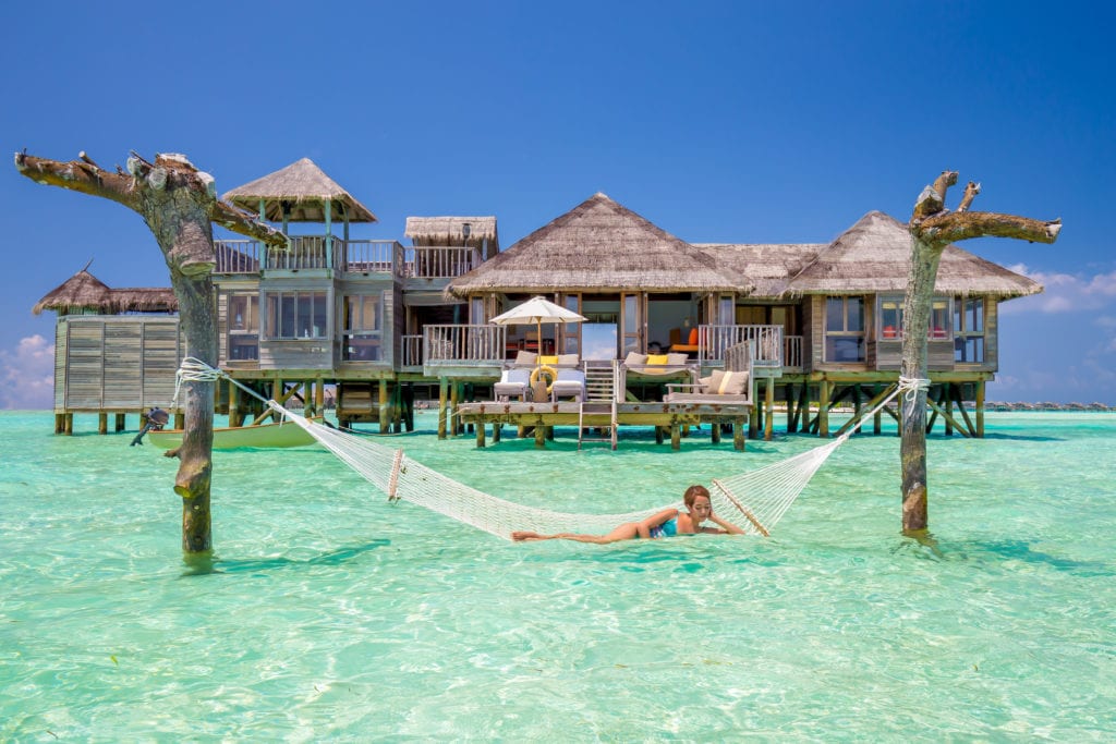 A woman relaxing on a white net hammock suspended over turquoise ocean water at Gili Lankanfushi luxury resort, Maldives – perfect for a romantic honeymoon photo.