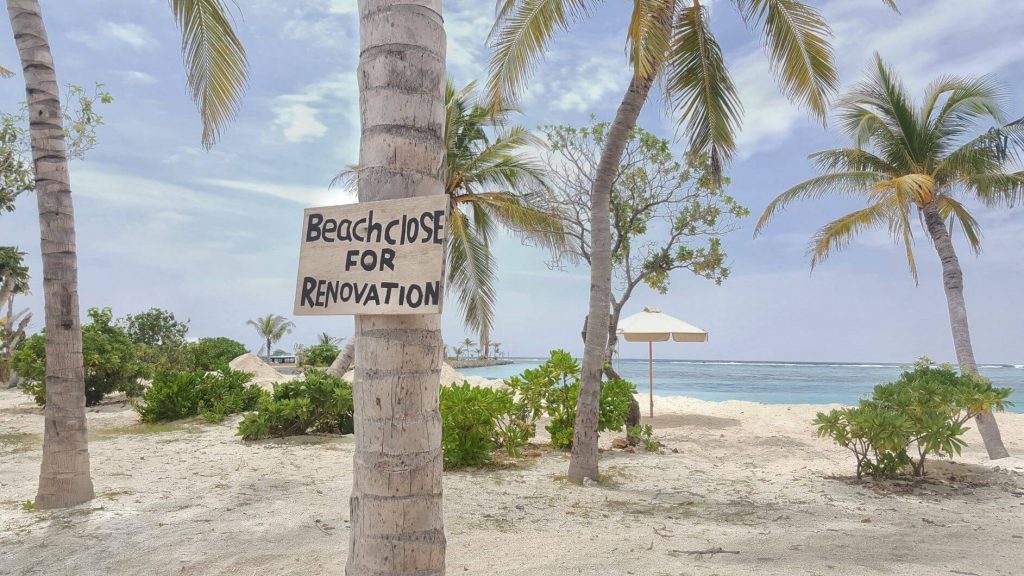 A wooden sign on a palm tree saying "Beach Close For Renovation" at a tropical resort in the Maldives.