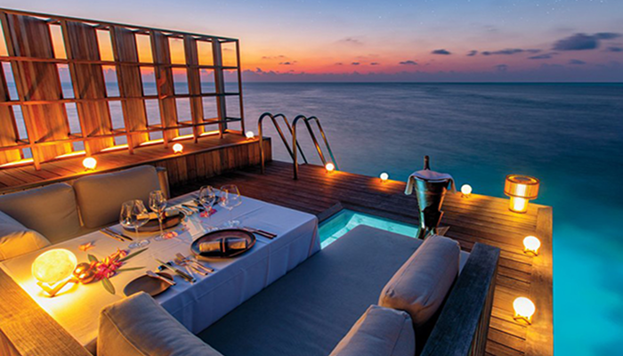 Romantic overwater private dinner setup at sunset in a Maldives luxury resort for honeymoon couples.
