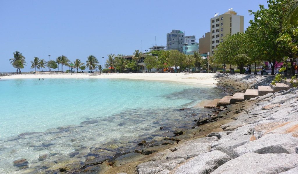A panoramic view of the Artificial Beach in Malé City, Maldives, showing turquoise water, white sand, and the city skyline—a top photography spot in the Maldives.