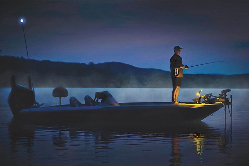 A fisherman standing on a boat during a night fishing excursion in the calm waters of Raa Atoll, Maldives, under a twilight sky.