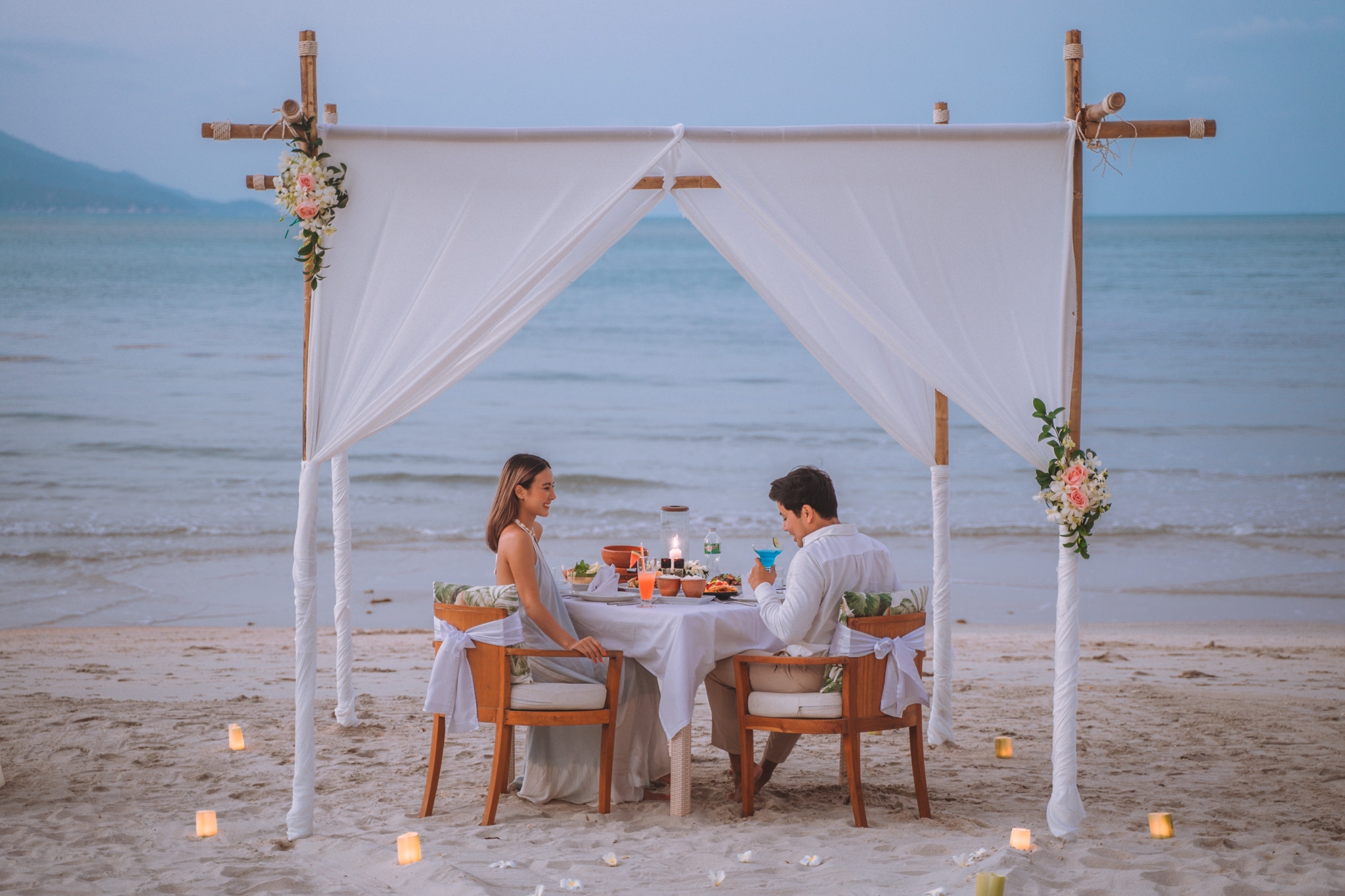 A romantic private candlelit dinner setup on a white sandy beach in Maldives during sunset for first-time visitors.