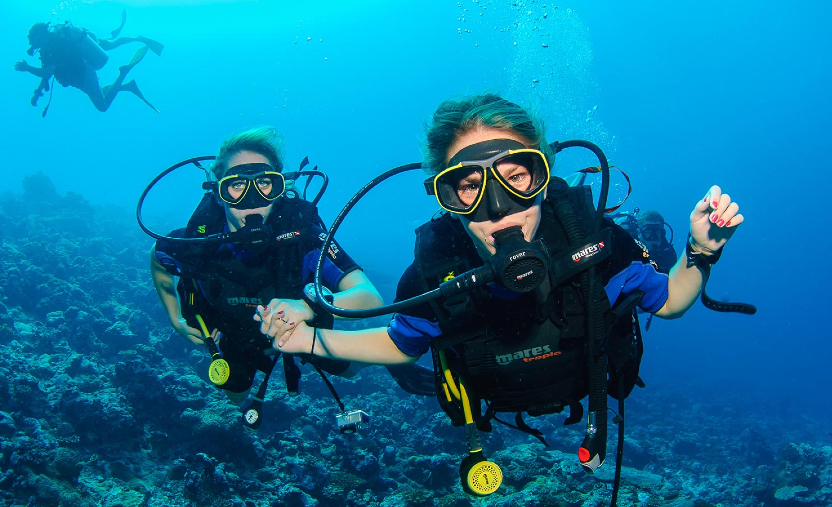 Two female scuba divers holding hands and exploring a coral reef in the Maldives crystal clear blue water.