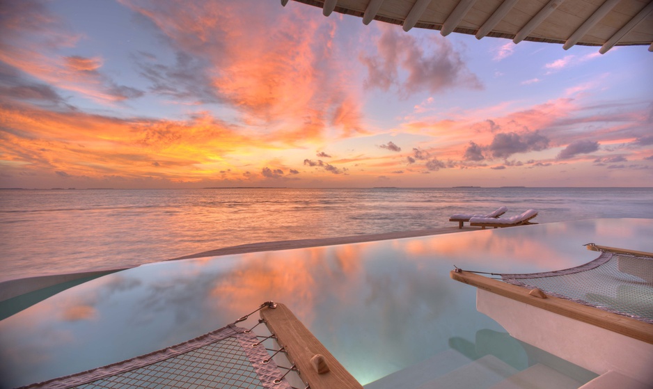Luxury overwater villa at Soneva Jani Maldives with a private infinity pool and hammock during a golden sunset.