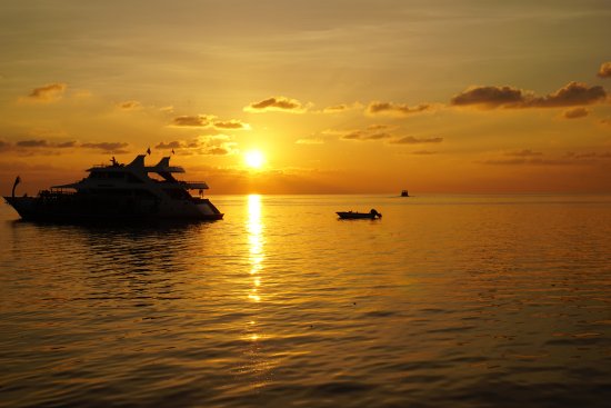A luxury safari boat and small dhoni at sunset in Vaavu Atoll, Maldives, reflecting golden light on the Indian Ocean.