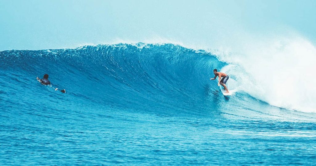 A professional surfer riding a perfect blue barrel wave in the Maldives, turquoise ocean background.