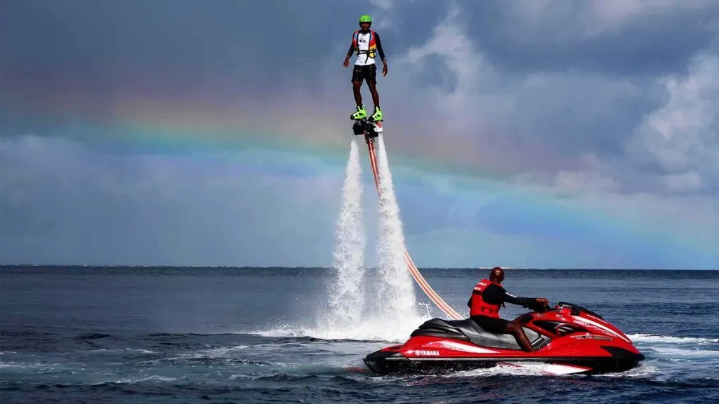 A person flyboarding high above the ocean with a rainbow in the background, powered by a jet ski in Vaavu Atoll, Maldives.