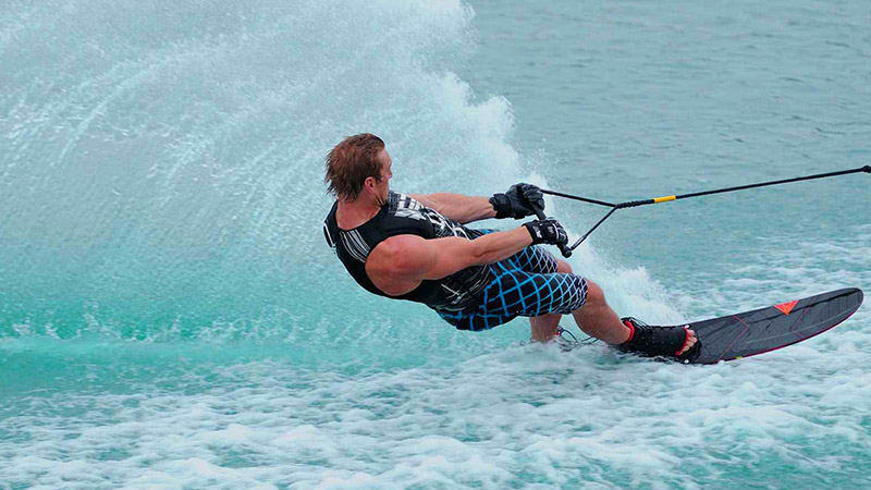 A man water skiing on the turquoise waters of Raa Atoll, Maldives, creating a large spray of water.