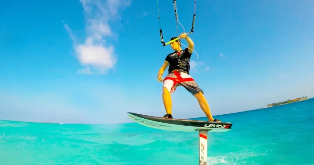 A man kitesurfing on a hydrofoil board over clear turquoise waters in the Maldives under a bright blue sky.