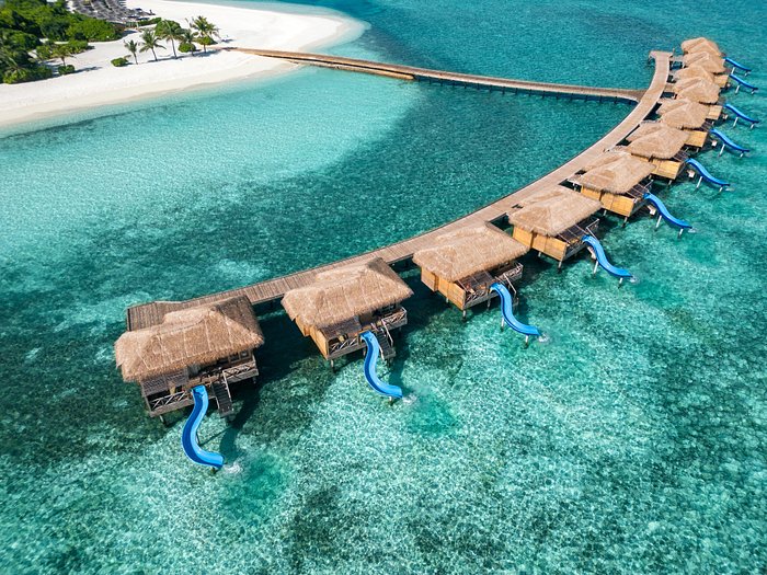 Aerial view of luxury overwater villas with private slides at an adults-only honeymoon resort in the Maldives, surrounded by turquoise ocean water.