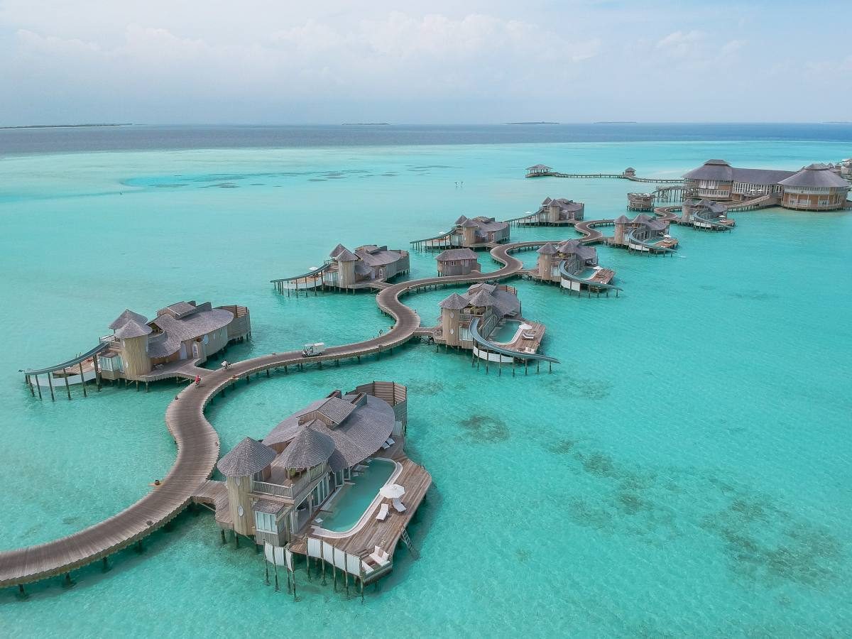 Panoramic view of luxury overwater villas connected by a wooden boardwalk over turquoise crystal clear water in a Maldives resort during golden hour.