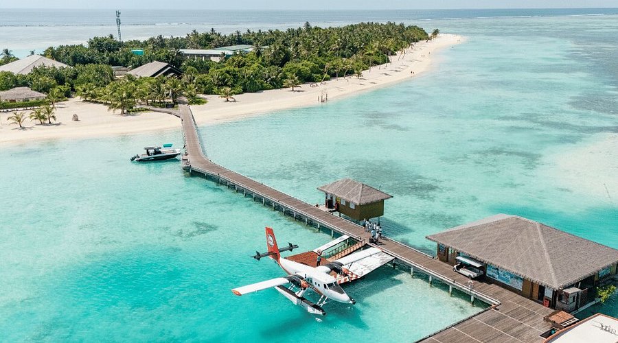 Aerial view of a seaplane docked at a wooden jetty of a luxury resort in Lhaviyani Atoll, Maldives, surrounded by turquoise lagoons and white sandy beaches.