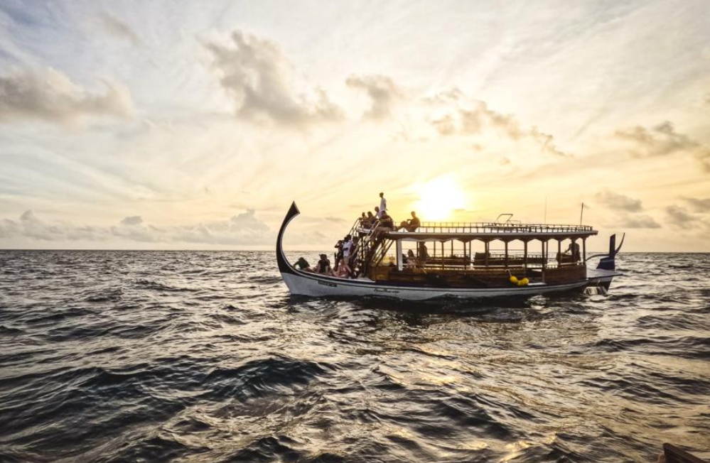 A traditional Maldivian dhoni boat during a sunset dolphin cruise in Laamu Atoll, showcasing the vibrant marine life and ocean wildlife trips.