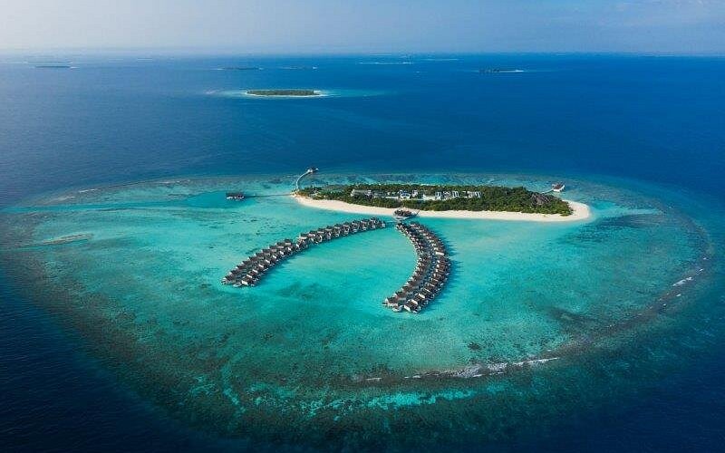Aerial view of overwater villas at Mövenpick Resort Kuredhivaru in Noonu Atoll, Maldives, surrounded by turquoise lagoon and coral reefs.