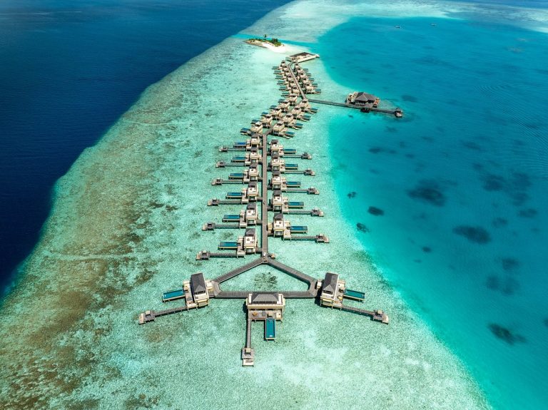 Aerial view of luxury overwater villas and turquoise lagoon in Meemu Atoll, Maldives, showcasing an untouched island escape.