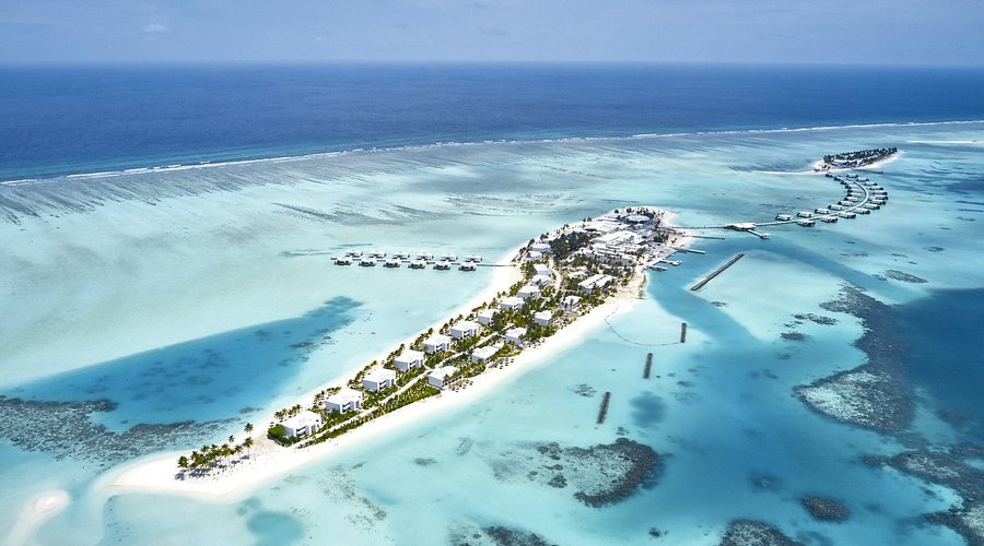 An aerial panoramic view of Riu Palace Maldivas luxury resort featuring white sand beaches, turquoise lagoons, and overwater villas in Dhaalu Atoll, Maldives.