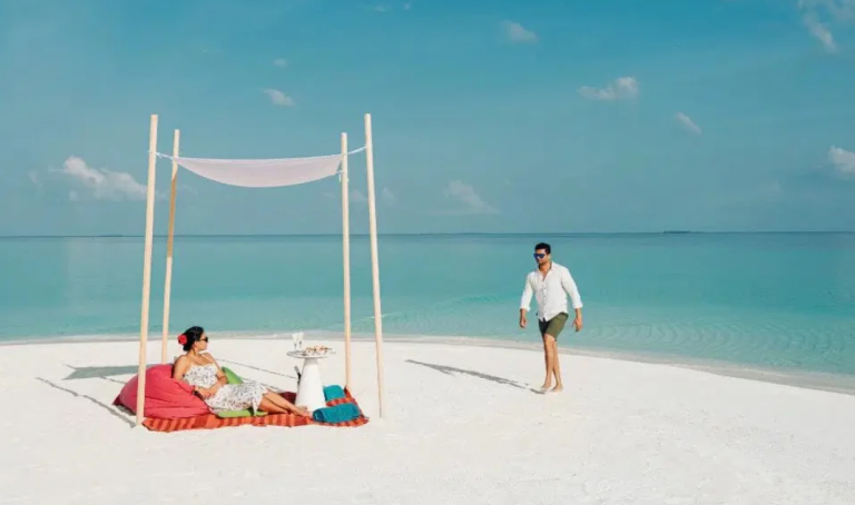 A couple enjoying a private sandbank picnic on a white sand beach in Laamu Atoll, Maldives, with turquoise ocean water.