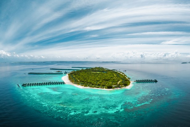Aerial view of Siyam World Maldives luxury resort in Noonu Atoll featuring overwater villas, turquoise lagoons, and lush tropical greenery under a blue sky.