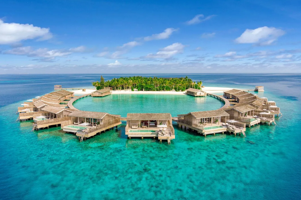 Aerial view of luxury overwater villas arranged in a circle over turquoise water at a resort in Dhaalu Atoll, Maldives.