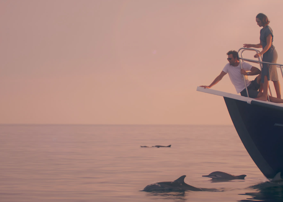 A couple watching dolphins during a sunset cruise in Dhaalu Atoll, Maldives.