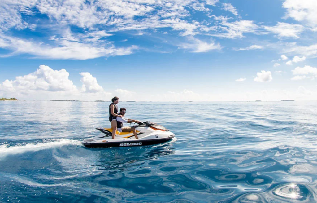 A couple enjoying a high-speed jet ski ride on the crystal clear turquoise water of Dhaalu Atoll, Maldives.