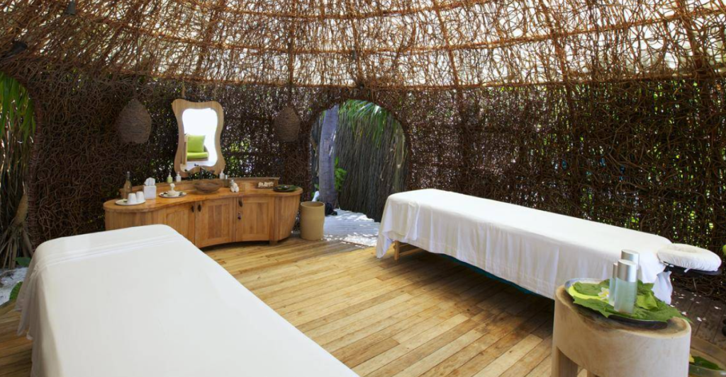 A luxury eco-friendly spa treatment room in Laamu Atoll Maldives featuring woven twig walls, wooden flooring, and two massage beds for a wellness retreat.