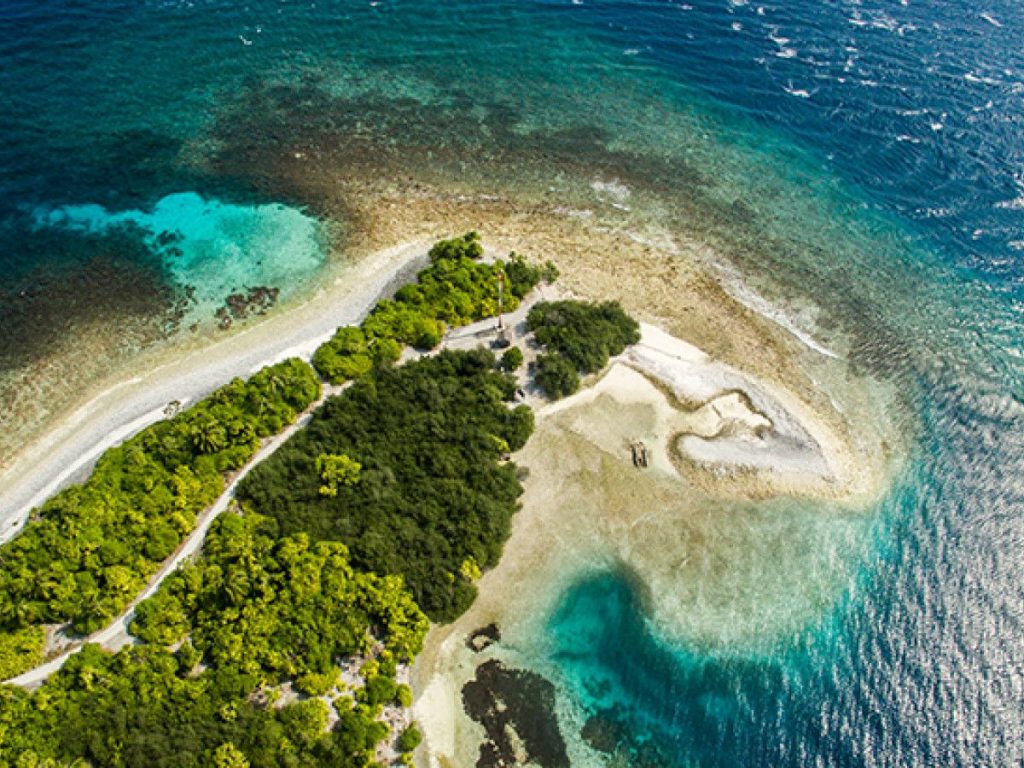 An aerial view of a small island in Addu Atoll, Maldives, highlighting the green trees and the surrounding coral reef.