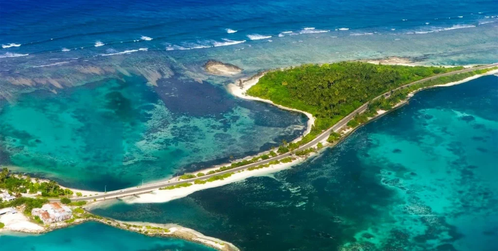 An aerial perspective of a tropical island in Addu Atoll, Maldives, showing turquoise lagoons, a scenic coastal road connecting islands, lush greenery, and the potential location of luxury water villas. This image visualizes the natural beauty that attracts visitors seeking top-tier resorts.