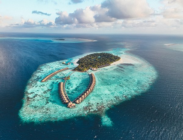 An aerial drone shot of a luxury island resort in Gaafu Dhaalu Atoll featuring overwater villas, turquoise lagoons, and lush tropical greenery under a cloudy sky.