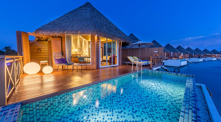Sunset view of a luxury overwater pool villa at Mercure Maldives Kooddoo Resort in Gaafu Alifu Atoll, showing a private infinity pool and thatched-roof architecture.