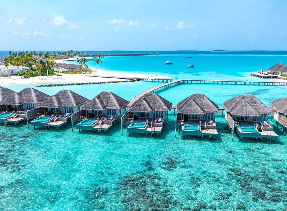 Drone view of luxury overwater bungalows with private pools near Maafushi Maldives. Crystal clear turquoise water and coral reef visible. Accessible by speedboat. Part of a curated list of top resorts near Maafushi without seaplane transfers.