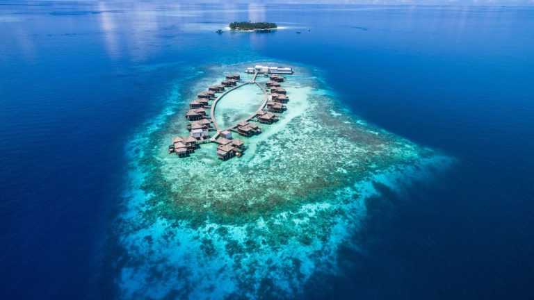 Aerial drone shot of Raffles Maldives Meradhoo overwater villas and pristine house reef in the Southern Maldives.