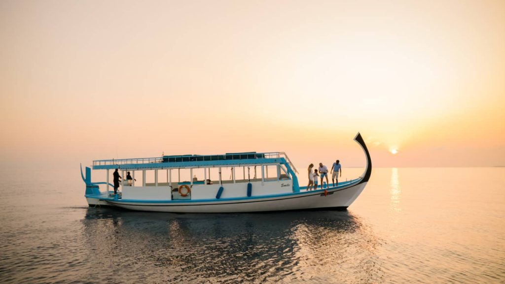 A traditional Maldivian Dhoni boat carrying tourists during a golden sunset cruise in Gaafu Dhaalu Atoll.