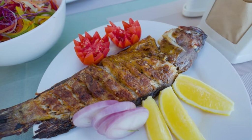 A sudden burst of charred sweetness comes from the fish, cooked next to the tender tentacles pulled fresh that morning. Each bite shifts between soft give and crisp edge, shaped by fire and sea alike.

Out here, they press spicy Maldivian paste deep into the fish - worked through the cuts scored along its sides so every part catches flavor. Fire roars underneath as it cooks, blackening the skin while holding tenderness within. Slice open, and instead of breaking apart like typical white fish, it resists slightly, thick and solid like land animal muscle. The taste? Bright and mild from coral waters, sharpened gently by what clings to it - not buried under spice, just lifted.

Wrapped in foil, then grilled - the grouper from that extra catch keeps every drop of juice inside. This fish stands out in the sea's lineup, its soft layers staying intact thanks to the gentle steam trap of aluminum. While sweet lips bring firmness and a satisfying chew, here the grouper leans into silkiness, unfolding deeper tastes with each bite. Cooked slow under radiant heat, its flavor blooms quiet but full.

Out here, just after noon heat fades, one catch sizzles next to another over open flame near the shore. Each bite tells how much comes from a single line dropped into coral waters.