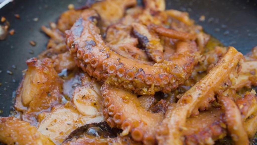 Back at Lua Beach Inn, the octopus from the morning catch got cooked the way locals have always done it. That old-style cooking makes all the difference in how it tastes. Knowing what goes into it explains exactly why it turns out that well. Start by softening the octopus - boil it, then freeze it overnight if there is enough time. The heat loosens tight muscle tissue; meanwhile, ice changes the cell makeup so the meat turns softer. A traditional approach seen among coastal residents involves striking the creature on rocks at shore to begin breaking it down prior to heating, yet for visitors staying in small seaside lodgings, simmering followed by freezing remains the usual path. After softening, pieces are sliced from the body while leaving most tentacles whole - appearance matters here. Roasted curry paste mixes with salt, pepper, and plenty of chilli flakes to form the coating. Not just sitting on top, the spices seep deep as time passes. That slow soak builds a core taste able to withstand high cooking temperatures. A sizzling skillet waits, oil shimmering under flame. Onions tumble in, softening slowly into sweet perfume. Marinated octopus follows, slipping between rings of translucent white. Heat kisses the surface, drawing out deep bronze along the edges. Caramelised drips cling where spice meets fire. Each bite yields easily, never rubbery, packed through and through with savour. Char lingers at the tips, proof of fierce contact. Inside stays supple, built on layers soaked long before the flame ever touched. What happens when you eat it? Nothing less than outstanding. Right on point is the texture - something many miss with octopus, but not here. Giving way easily, it takes in every bit of the marinade's taste. A slow-building heat from the chili shows up at the end, gentle instead of sharp.