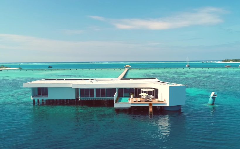 Spending actual hours here first makes sense - the part of the Muraka that sits above water already feels like a top-tier room at any regular hotel. After all, most places would call this setup their best option.
The Main Living Area
A massive open lounge takes up the main area above water, built for gathering and relaxing. One wall holds an 80-inch screen as its focal point. Instead of just sitting idle, a PlayStation 5 waits nearby for active play. Control flows through an iPad, managing light, heat, and functions across the home. What makes it different isn’t gloss or grandeur - it’s how warm, intentional, and truly used it seems compared to cold, cookie-cutter luxury.
The Bar and Welcome Amenities
Over in a corner of the living space, there’s a personal bar set up with enough glasses to serve quite a crowd. Below it, the minibar comes with the room price but holds just non-alcoholic drinks while alcohol costs extra - enough to give high-end guests pause. Still, they do offer a single bottle of champagne when you arrive and that helps balance things out.
White chocolate shaped like coral sits beside dates, neatly placed, a small treat waiting at first glance. A handwritten message from the top manager adds a personal touch, friendly even if expected. Though it lacks surprises in wording, the warmth comes through anyway. Oddly enough, the staff did not check who the traveler was before they came, skipping any background look-up. Some guests might enjoy that lack of attention, liking the quiet privacy instead.
A note about coffee: there’s tea and coffee setup available, also the kettle looks spotless. That said, the coffee maker comes empty - no beans inside - and reeks faintly of old milk. When you’re paying this much, tiny flaws like these become harder to ignore.
The Professional Kitchen
Inside The Muraka sits a kitchen built for pros, tools and appliances all ready. Missing from that setup? A cook to bring it to life. Hiring a private chef can be arranged separately, costing anywhere from three hundred to six hundred dollars each time - price shifts probably tied to how fancy the menu gets. Should you want something bold on the plate, say lobster or caviar, expect extra charges piling on top.
Facing the sea, the dining table sits just right for guests to see the waves while eating food made by a cook. Meals appear here, set out carefully, each plate tied to the rhythm of tides outside.
Outdoor Terraces and the Infinity Pool
Out here, two separate terraces offer their own kind of space. Facing south, one opens onto views of the larger Conrad complex, linking you gently to what's beyond your immediate spot. Then there’s the ocean-side deck - built around a pool that seems to spill right into the sea line. Down a short flight of steps, swimmers touch saltwater without detours. That option waits for anyone drawn more to waves than concrete edges.
The Above-Water Bedroom Suite
Up top, the main bedroom comes before the other two inside the Muraka. Skip the lower suite entirely - this room still stands out. Marble covers the private bathroom, where the shower feels like standing under a storm sky. There’s a Japanese Toto toilet tucked in here, the kind that shows up only where details matter most, so it gets mentioned every time.
A glass wall wraps around the bathroom, so being seen is hard to avoid. Some visitors feel free because of it, while others shift uneasily under the openness. Arriving unprepared might lead to surprise.
A space just beyond the bath holds a roomy closet plus a personal grooming station with plenty of shelves. Nearby lies a sleeping area meant for visitors, tucked away so it feels separate from the primary retreat. A small fitness spot follows next, an uncommon feature few stilted bungalows - no matter how costly - ever provide.